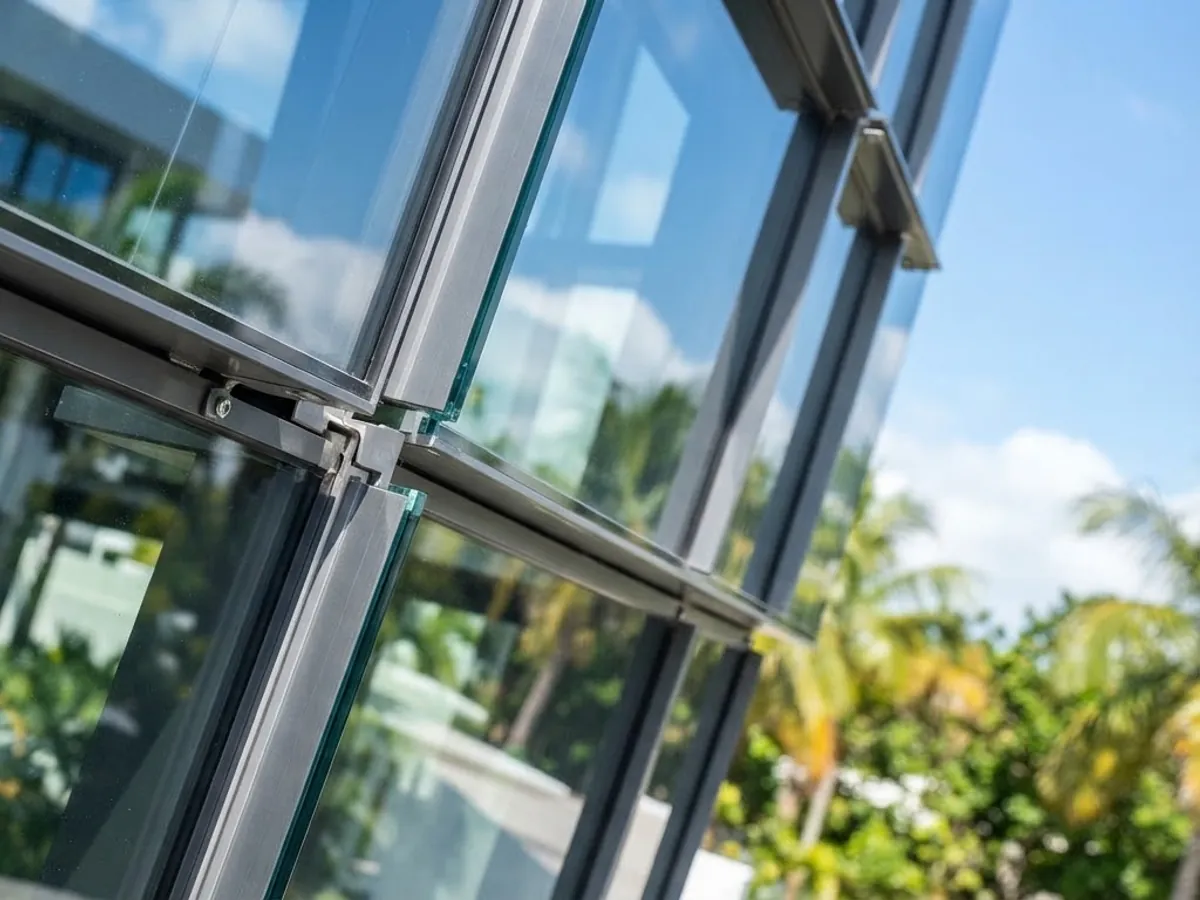 Glazed façade corner with structural fittings, photographed against tropical planting.