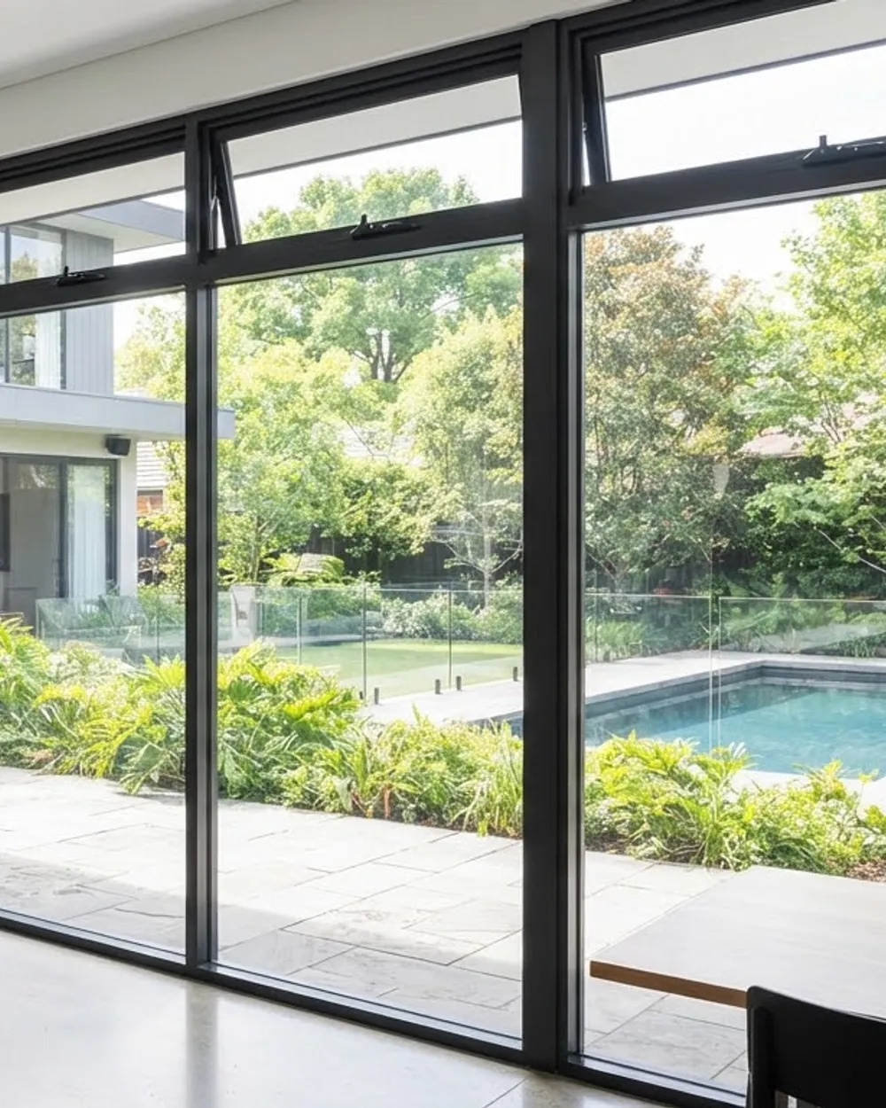 Full-height glazed screen in a slim aluminium frame dividing an interior from a garden.